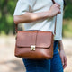 Person holding a brown leather bag outdoors